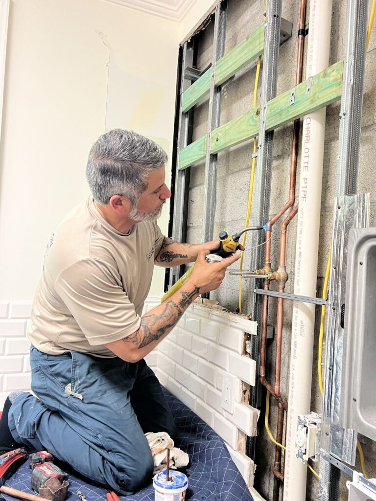 Plumber soldering copper supply lines inside an open wall during a repipe